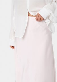 Jupe en satin rose clair avec une texture lisse et une coupe droite, associée à une chemise blanche légèrement transparente à boutons.