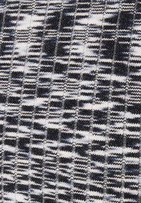 Tessuto texturizzato in nero, bianco e grigio con un motivo di righe e quadretti alternati. Materiale a maglia morbido con fibre visibili.