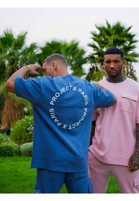 Blauw oversized kortemouwen shirt met cirkelvormige witte tekst op de achterkant, gecombineerd met een roze kortemouwen shirt met een voorkant pocket.