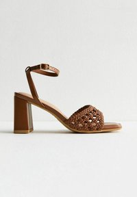 Brown woven heeled sandal with a square toe, adjustable ankle strap, and a solid block heel. Smooth sole and textured upper.