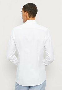 Weißes Langarmhemd mit klassischem Kragen, glatter Textur und abgerundetem Saum, das ein schlichtes und sauberes Design präsentiert.