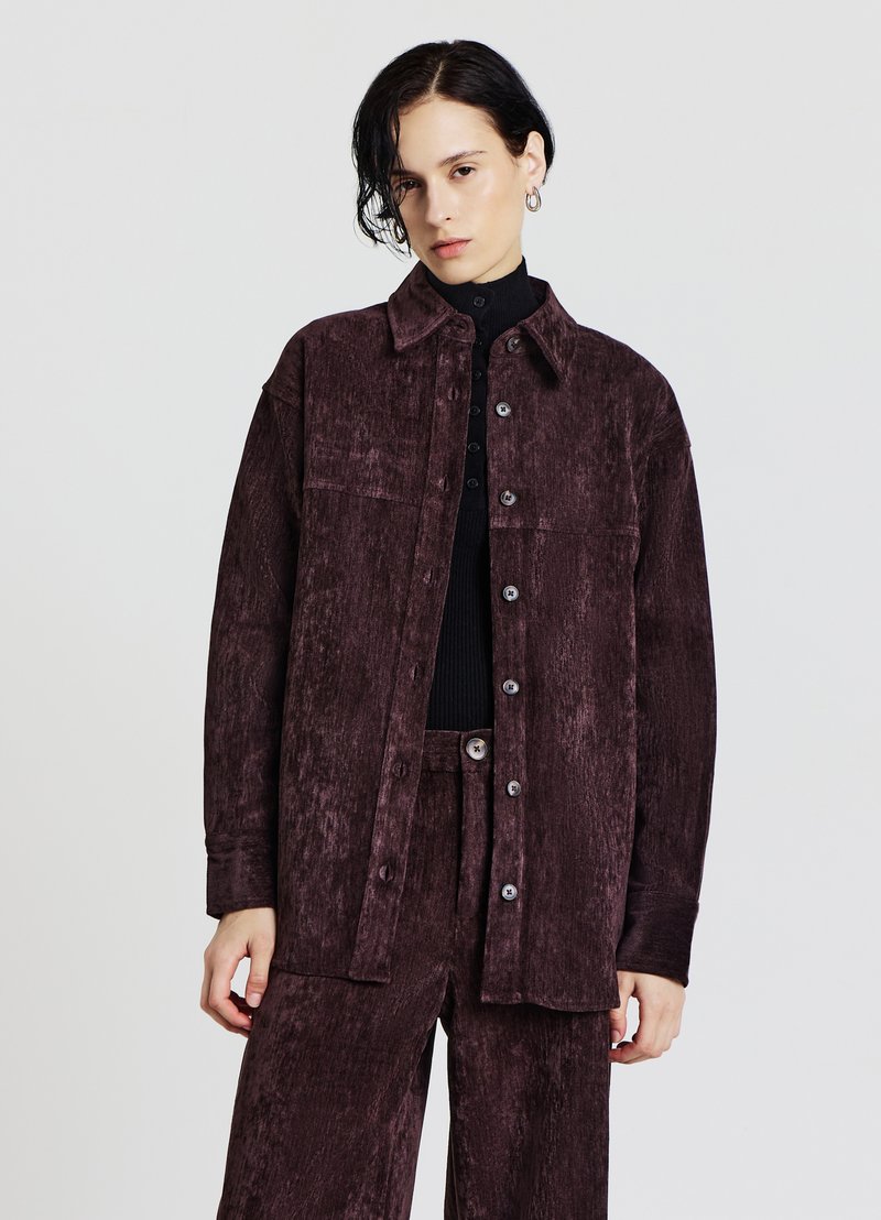 Camicia in velluto a coste color granata con chiusura frontale con bottoni, collo ampio e maniche lunghe, caratterizzata da una finitura testurizzata e una sottile lucentezza.