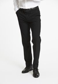 Zwarte op maat gemaakte broeken met een rechte pasvorm, subtiele textuur en voorplooien. Gecombineerd met zwarte leren dresschoenen en een wit shirt.