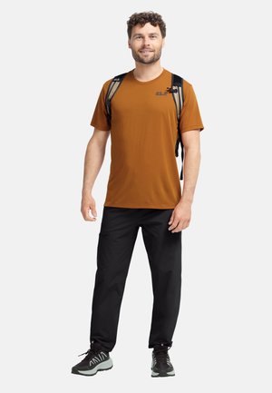 Bruin T-shirt met korte mouwen, zwarte cargobroek en grijze sneakers. Rugzak met twee banden. Glad materiaal en comfortabele pasvorm.