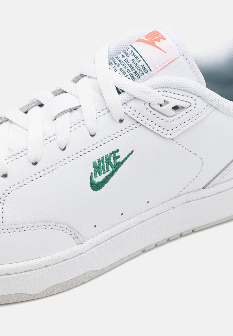 Baskets blanches avec logo Nike vert, dotées d'un dessus en cuir, de lacets texturés, d'un col rembourré et d'une semelle en caoutchouc. La languette affiche la marque.