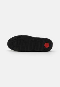 Svart sneaker sula med texturerad yta, med präglat varumärke och en röd cirkulär accent. Mönster för grepp.