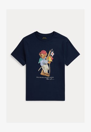 Maglietta blu navy con un orsacchiotto vestito in abiti casual e un berretto rosso che tiene bandiere del segnale nautico e una corda.