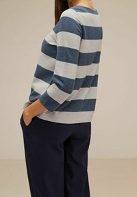 Blå och grå randig tröja med trekvartslånga ärmar, mjuk textur och ribbade manschetter, matchad med mörk marinblå byxor.