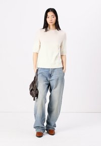 Helles Cremefarbenes kurzärmliges Strickoberteil, lockere blaue Jeans, braune Stiefeletten und eine dunkelbraune Umhängetasche. Schlichte und lässige Passform.