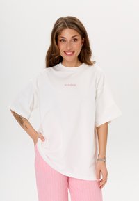 Witte oversized t-shirt met een ronde halslijn en korte mouwen, met roze "MIRONS" tekst op de borst. Soepele, lichte stof.