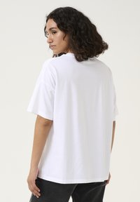 T-shirt en coton blanc avec une coupe décontractée, col rond et manches courtes. Texture lisse, design simple et forme légèrement surdimensionnée.