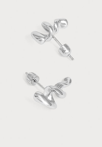 Paire de boucles d’oreilles clous en métal argenté torsadé avec fermoirs à poussoir sur un fond clair uni.