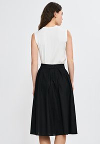 Czarna plisowana spódnica z dopasowanym pasem, wykonana z lekkiego materiału. Połączona z białą bluzką bez rękawów, z gładką fakturą.