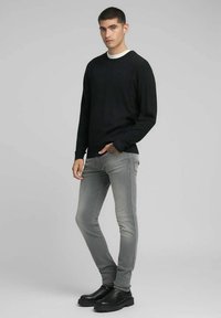 Grijze slim-fit jeans met gestikte zijdetails, gecombineerd met een zwarte trui met ronde hals en lange mouwen en zwarte enkellaarsjes.