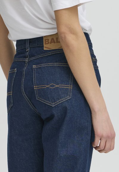 Jean en denim bleu à taille haute, avec deux poches arrière et une étiquette en cuir marron portant la marque "BAL". Détails de surpiqûres contrastées.
