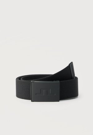 Cinturón de tela negra enrollado con una hebilla rectangular mate en negro que presenta un logo sutilmente en relieve sobre un fondo claro y liso.