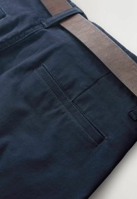 Sötétkék szövetnadrág sima textúrával, egy hátsó zsebbel és egy barna bőr övvel.