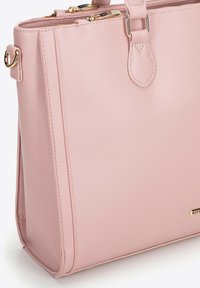 Rectangular light pink leather handbag with double handles, gold-tone hardware, top zippers, and subtle brand plaque on the front.