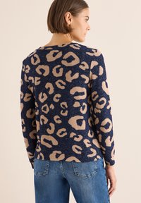 Pullover blu navy con una fantasia a leopardato in beige. Design aderente, maniche lunghe, texture morbida, indossato con jeans in denim.