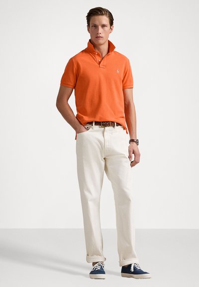 Orange polo skjorta med krage, vita byxor och blå canvas sneakers. Strukturerad textil och klassisk passform, med en logotyp på bröstet.