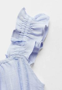 Vaaleansininen kangasmekko, jossa on poimutettu pinta ja röyhelökoristeet. Pehmeä, kevyt materiaali, jossa on rispaantuneet reunat ja joustavat yksityiskohdat.