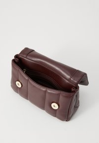 Pequeña bolsa de mano de cuero marrón oscuro acolchada con una solapa, dos botones de presión en tono dorado y un bolsillo interior con cremallera, mostrada abierta.