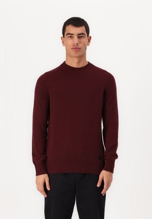 Burgundy crew-neck sweater made of soft fabric with ribbed cuffs and hem. Features a small black logo tag on the lower left side.