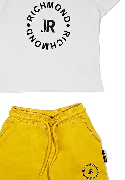 T-shirt bianca in cotone con logo circolare nero con la scritta "RICHMOND JR" sopra a pantaloni corti gialli in cotone con vita elastica e tasche laterali.