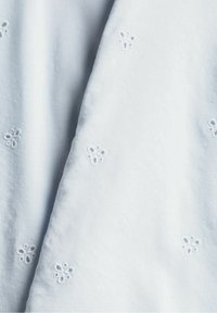 Tessuto blu chiaro con una texture morbida, caratterizzato da motivi floreali bianchi ricamati distribuiti uniformemente sulla superficie.
