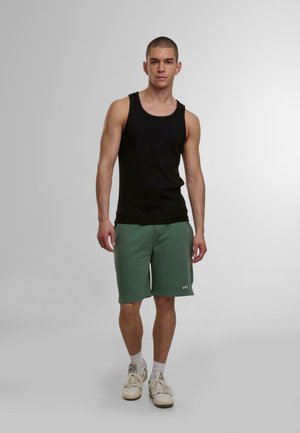 Black tank top paired with green sweatshorts, featuring an elastic waistband and side pockets. Footwear includes light-colored sneakers.