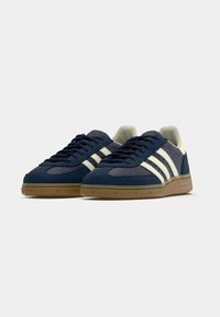 Marineblauwe sneakers met witte strepen, suède en gestructureerde panelen, een zool van gumrubber en een afgeronde neus. Voorzien van platte veters en een gewatteerde kraag.