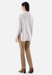 Helles beige Strickpullover mit hohem, geripptem Kragen. Kombiniert mit beigen Hosen und braunen Absatzstiefeln, die eine lässige Passform und strukturierte Stoffe zeigen.