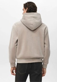 Hoodie in corduroy beige con un grande cappuccio strutturato, polsini e orlo a coste, abbinato a jeans scuri, che mostrano un look casual e rilassato.