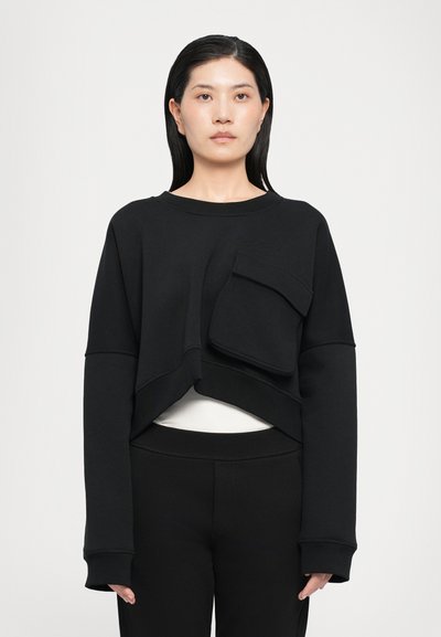 Schwarzer, kurzer Sweatshirt mit einer Fronttasche, langen Ärmeln und lockerer Passform, kombiniert mit hochgrätierten schwarzen Hosen. Glatte Stofftextur.