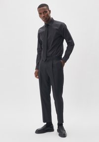 Conjunto de camisa y pantalones negros, que presenta un diseño ajustado, tejido suave, mangas largas y un corte recto, complementado con zapatos negros.