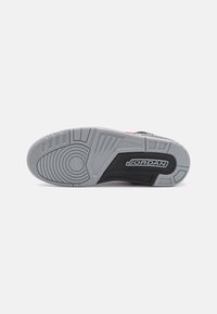 Semelle d’une chaussure de sport grise et noire avec le logo « JORDAN », avec des motifs de bande de roulement circulaires et rectangulaires pour la traction.