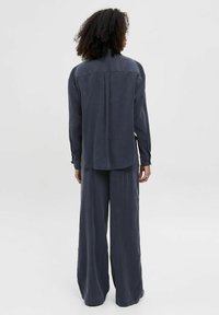 Mørkeblå to-piece outfit bestående af en langærmet skjorte med lige skæring og vide bukser. Blødt stof med mat finish.