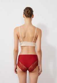 Beige polstret bralette med tynne stropper, kombinert med høyt midje rød truse med gjennomsiktige blonder og en solid stoff bak.
