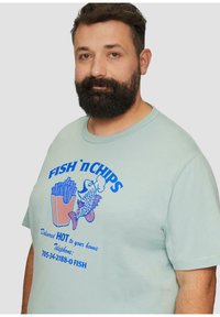 Jasnozielona bawełniana koszulka z niebieską grafiką przedstawiającą rybę i frytki z napisem. Okrągły dekolt, krótkie rękawy, luźny krój.