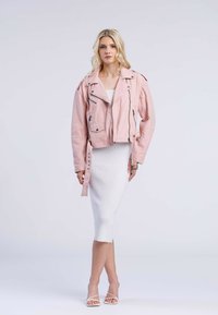 Rosa kort läderjacka med blixtlåsdetaljer och axelklaffar, bärs över en vit ribbad klänning, matchad med vita remsandaler.