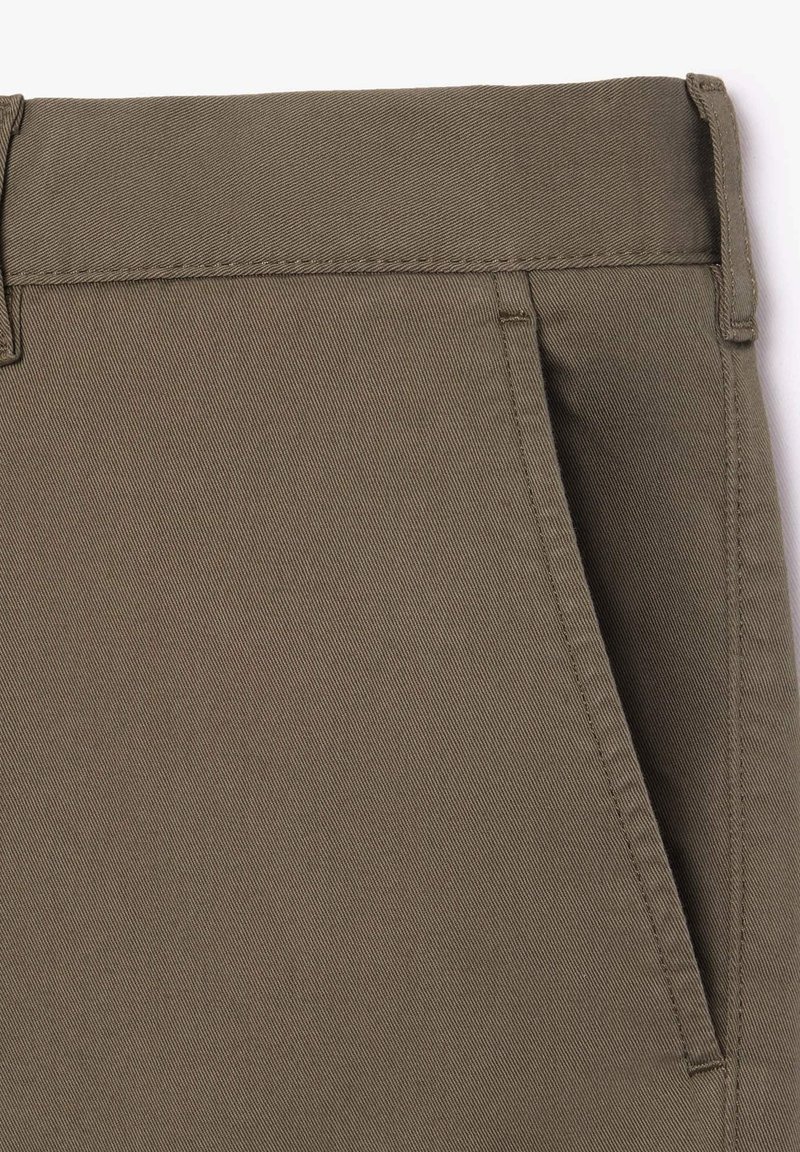 Pantalon khaki marron en tissu lisse et texturé, avec une taille plate et une poche latérale, mettant en valeur un design ajusté.