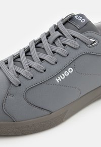 Grå sneakers med teksturert syntetisk overdel, flate grå lisser og subtil logo-detaling. Har en polstret såle for komfort.