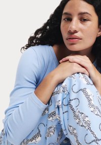 Haut à manches longues bleu clair avec texture côtelée ; associé à un pantalon bleu clair ornés d'un motif léopard en noir et blanc.