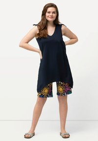 Tunica senza maniche blu navy con scollatura a V e dettagli con lacci sulle spalle, abbinata a pantaloni corti colorati con motivi solari. Calzature leggere.