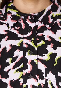 Painettu paita musta, valkoinen, vaaleanpunainen ja vihreä, jossa on kaulus, napit ja rintatasku, jossa on aaltoileva, abstrakti kuvio.