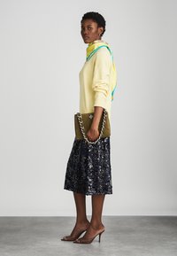 Olīvzaļš zamšādas rokassoma ar sudraba ķēdes siksnu, dzeltena adīta džemperis, tumši zilā sekvīnu svārki, brūnās augstpapēžu kurpes, šalle ar zilām akcentiem.