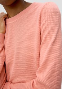 Pull pêche tricoté avec un motif texturé, col rond et manches longues. Poignets et ourlet côtelés ajoutent du détail au design.