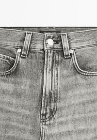 Graue Denim-Jeans mit hoher Taille, silbernem Knopf und kontrastierenden Nähten. Sie verfügen über eine Vordertasche und ein Etikett am Bund.
