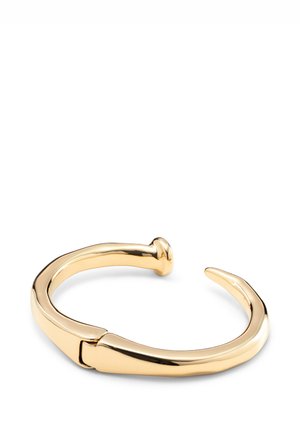 Bracelet manchette en métal ton or avec une finition lisse et brillante. Présente un design incurvé avec une extrémité pointue et un détail de fermeture arrondi.