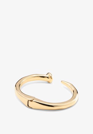 Brazalete de metal con tono dorado y acabado liso y brillante. Presenta un diseño curvado con un extremo puntiagudo y un detalle de cierre redondeado.